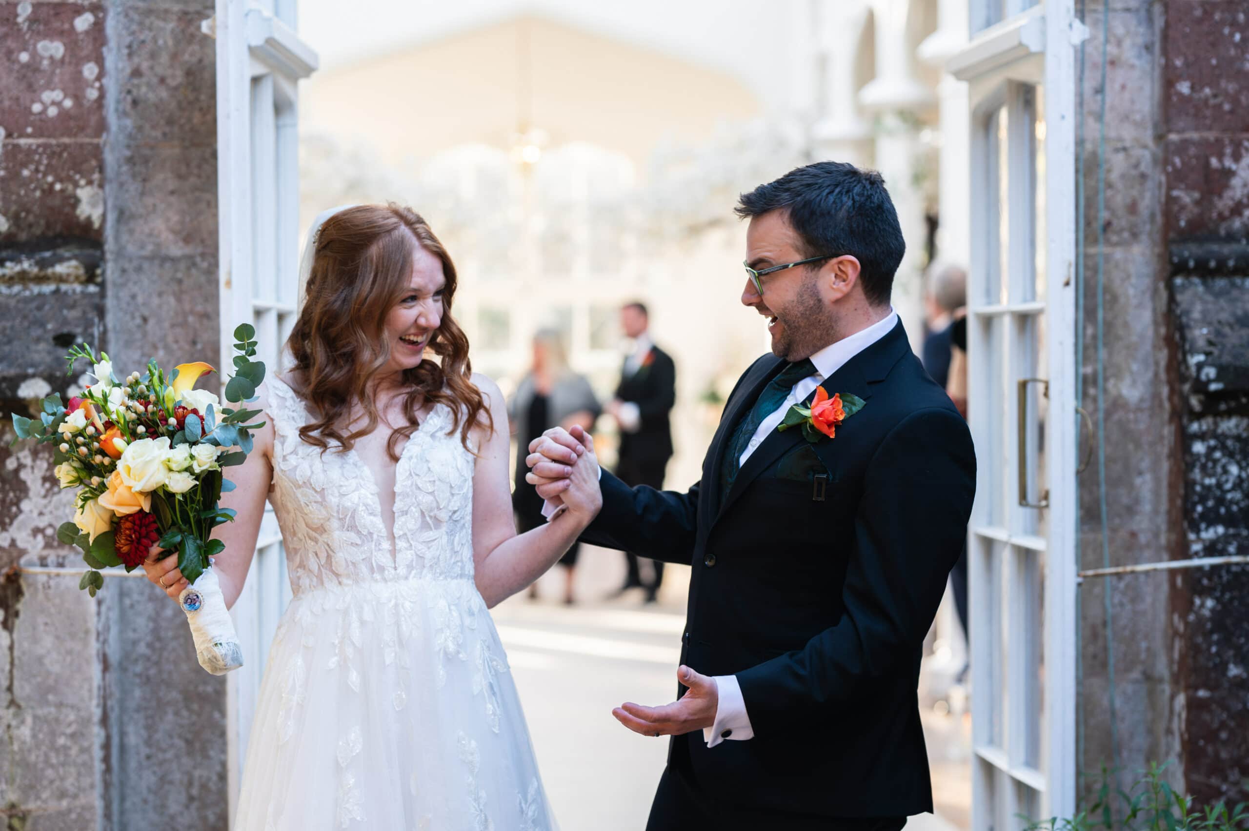 Bride and groom laugh together in the doorway of a glasshouse