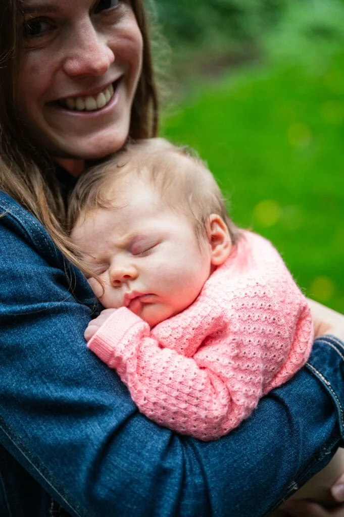Mum smiles as she cradles her sleeping baby in the garden