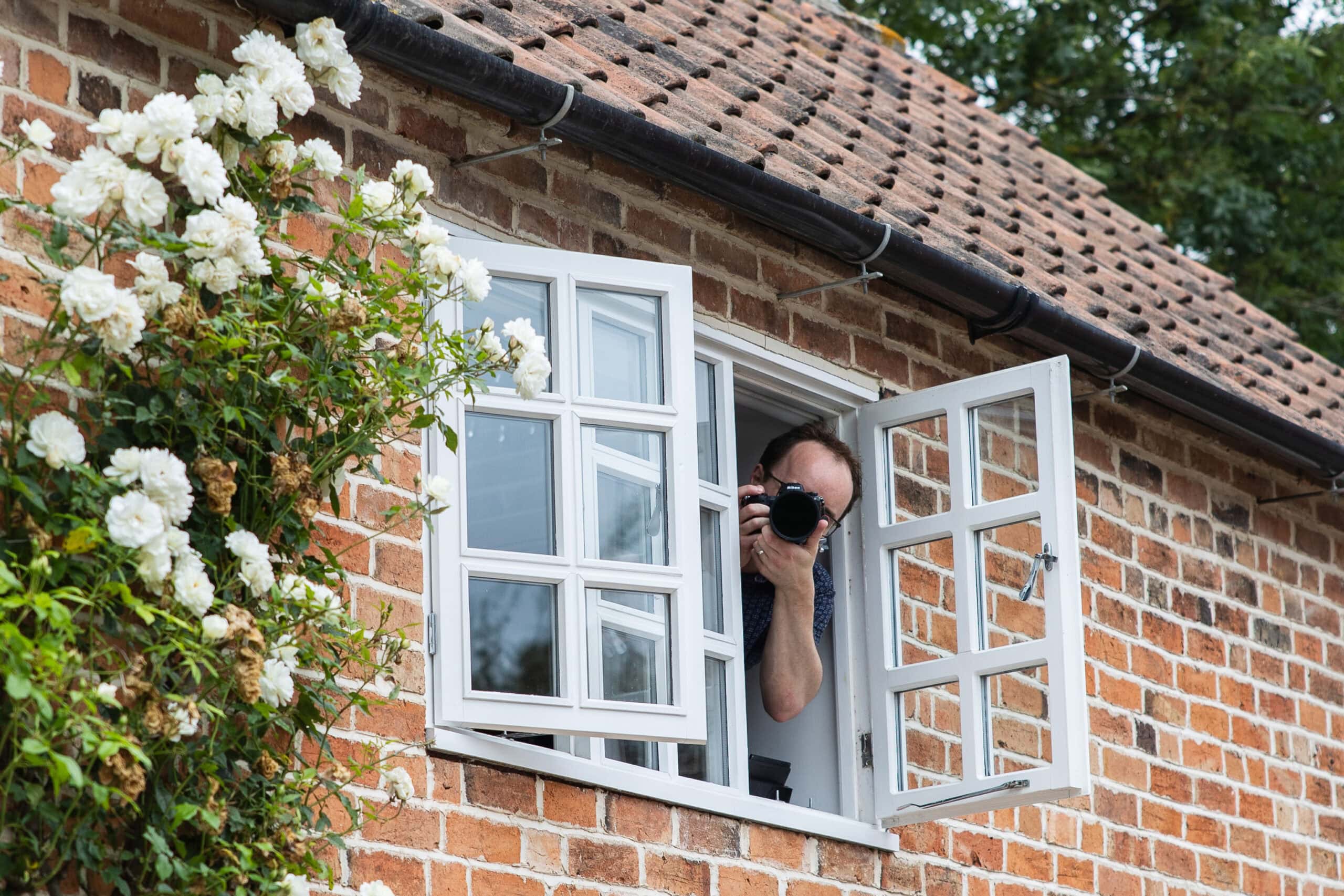 Photographer leans out of a cottage window with a camera during a photography lesson