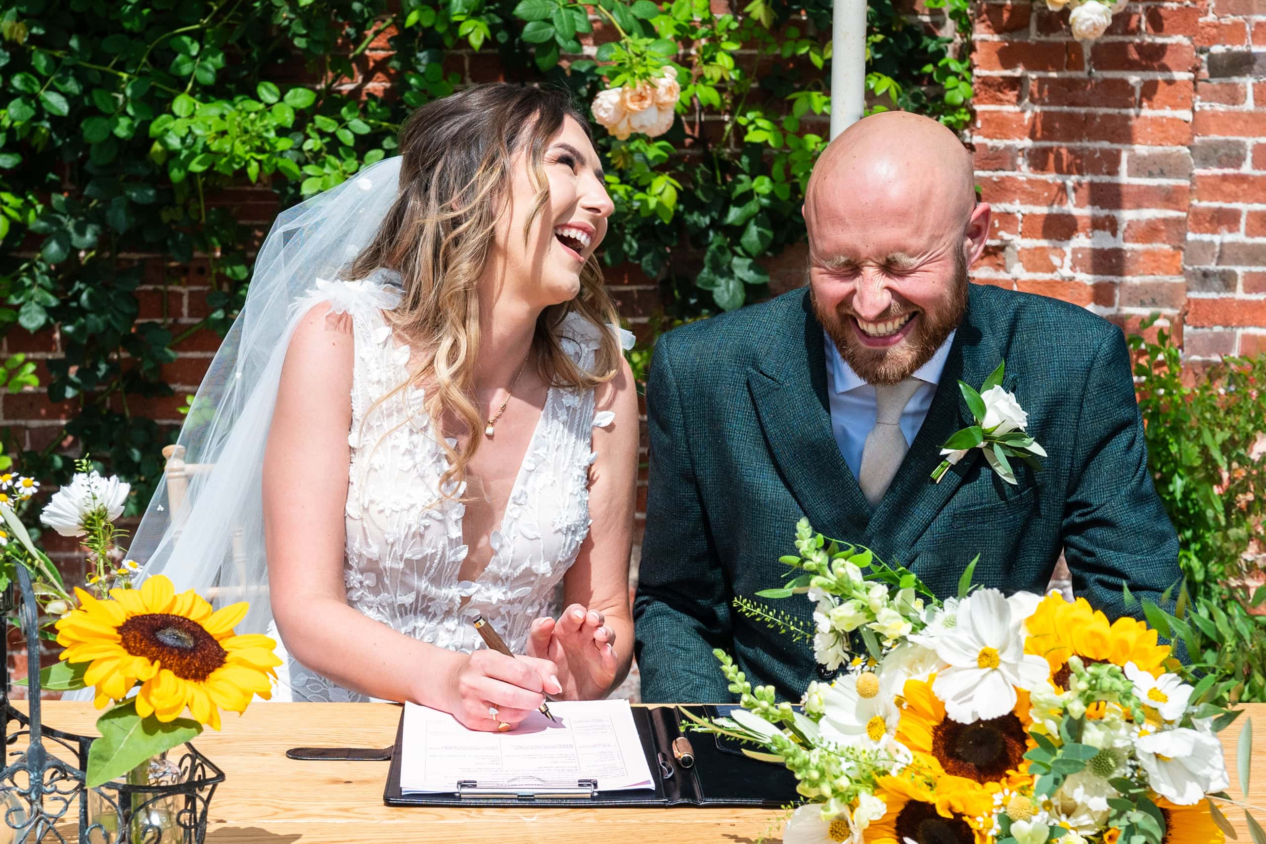 Bride and groom laugh during the signing of the wedding certificate.