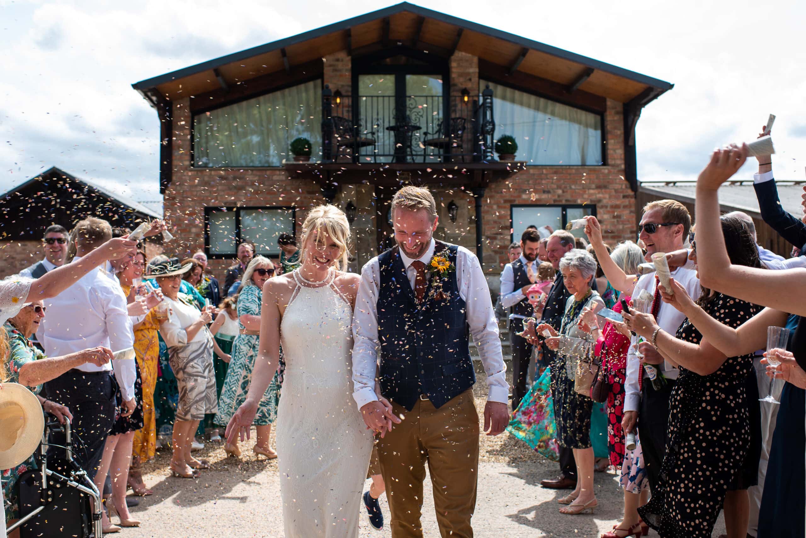 Bride and groom walk through confetti in front of the lodge at Willow Marsh Farm
