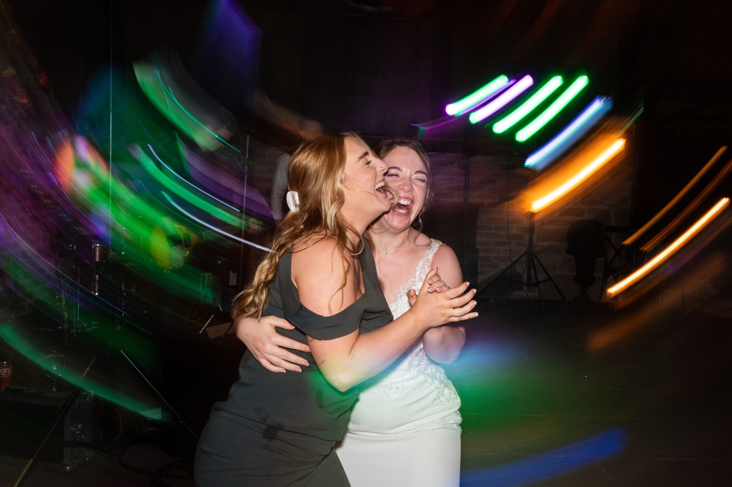 Bride dances with a friend under colourful lights at her Willow Marsh Farm evening reception