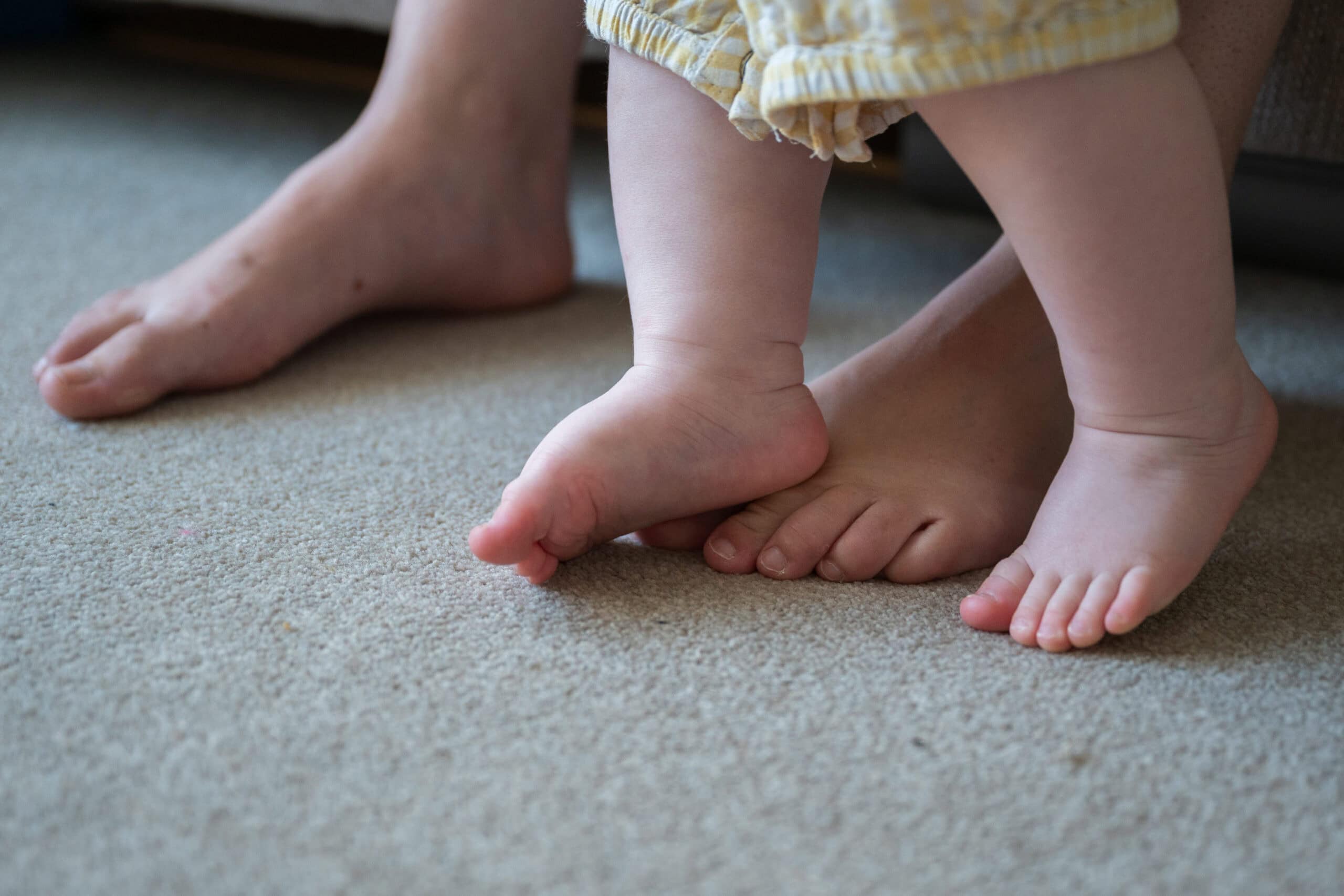 A toddler's bare feet on the carpet beside a parent's