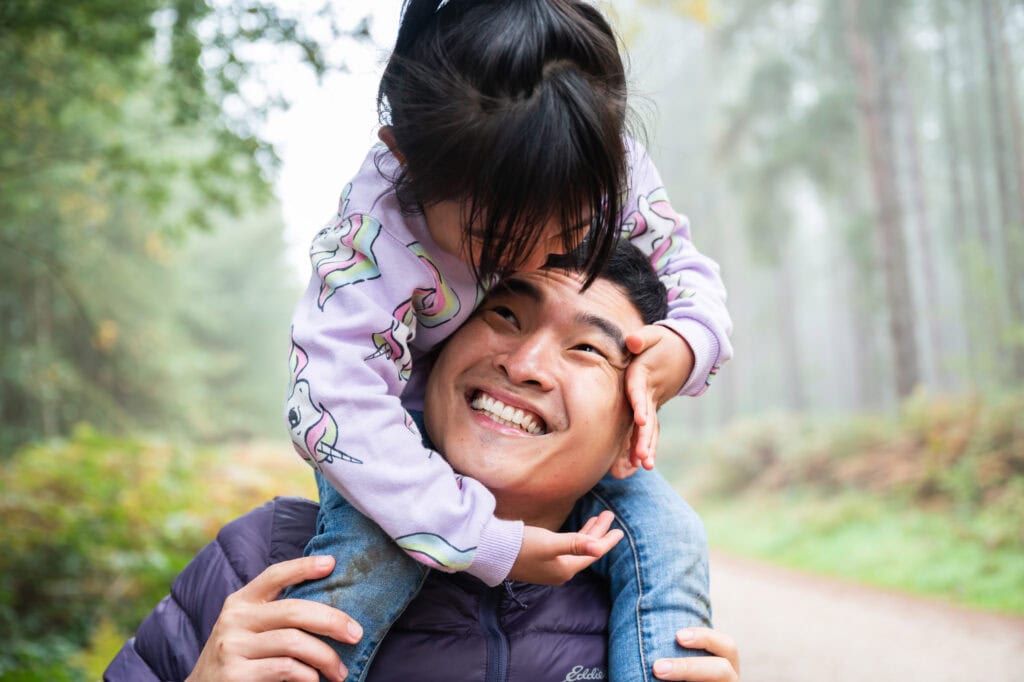 Dad laughs as his daughter rides on his shoulders through misty woods