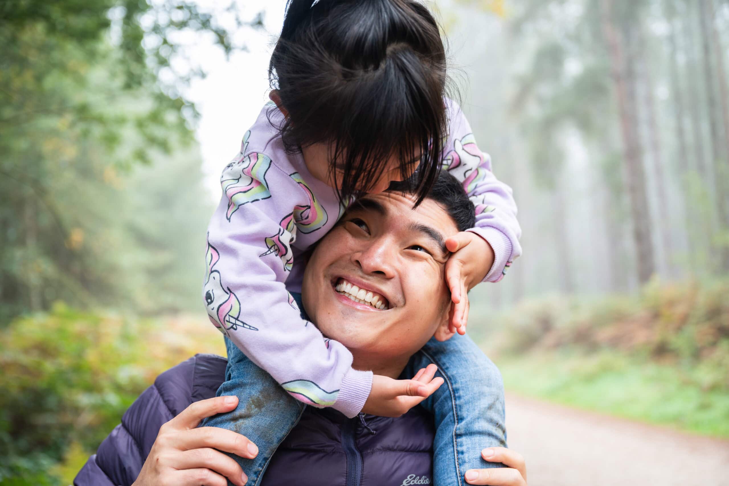Dad laughs as his daughter rides on his shoulders through misty woods
