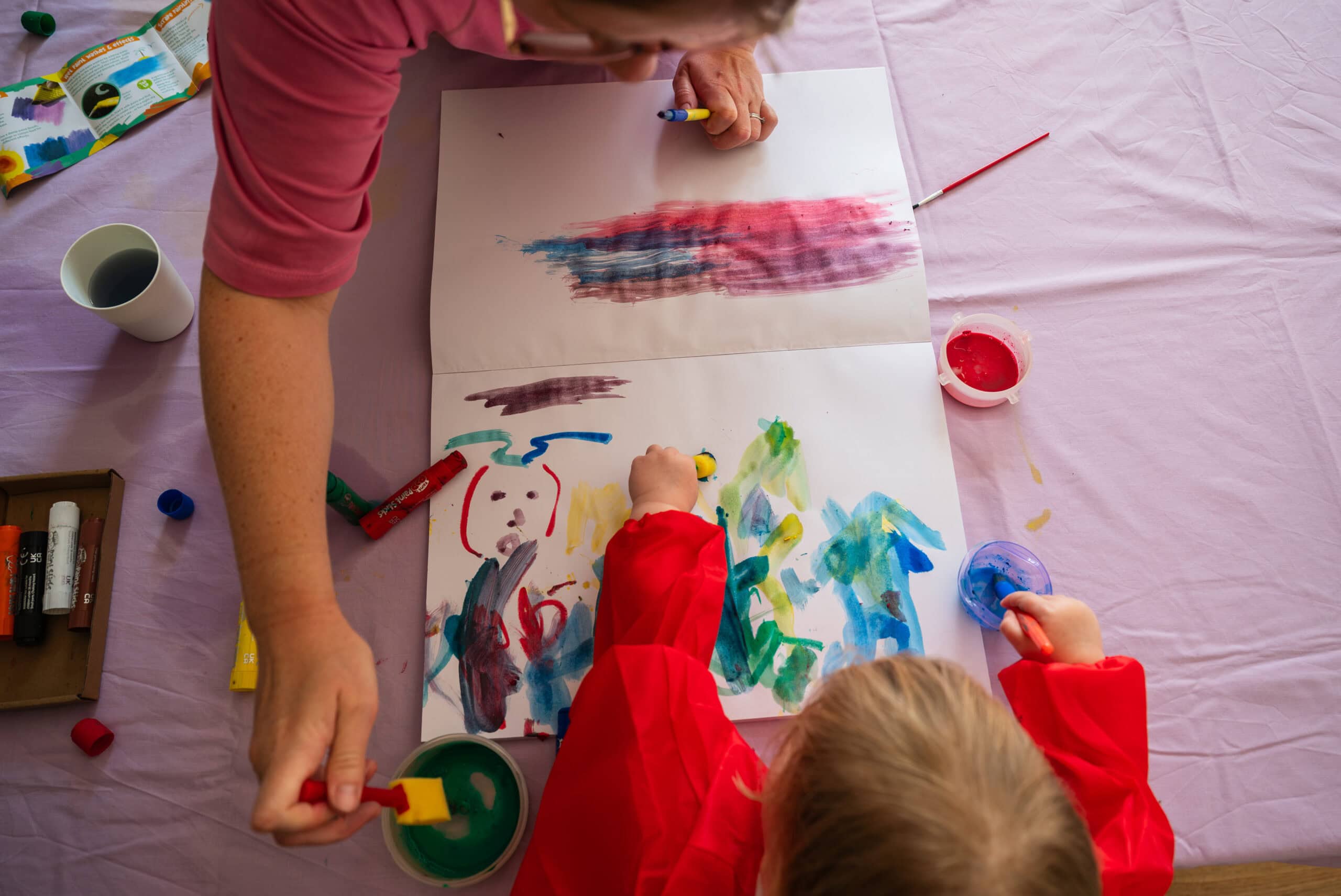 A toddler paints a picture with mum at the kitchen table