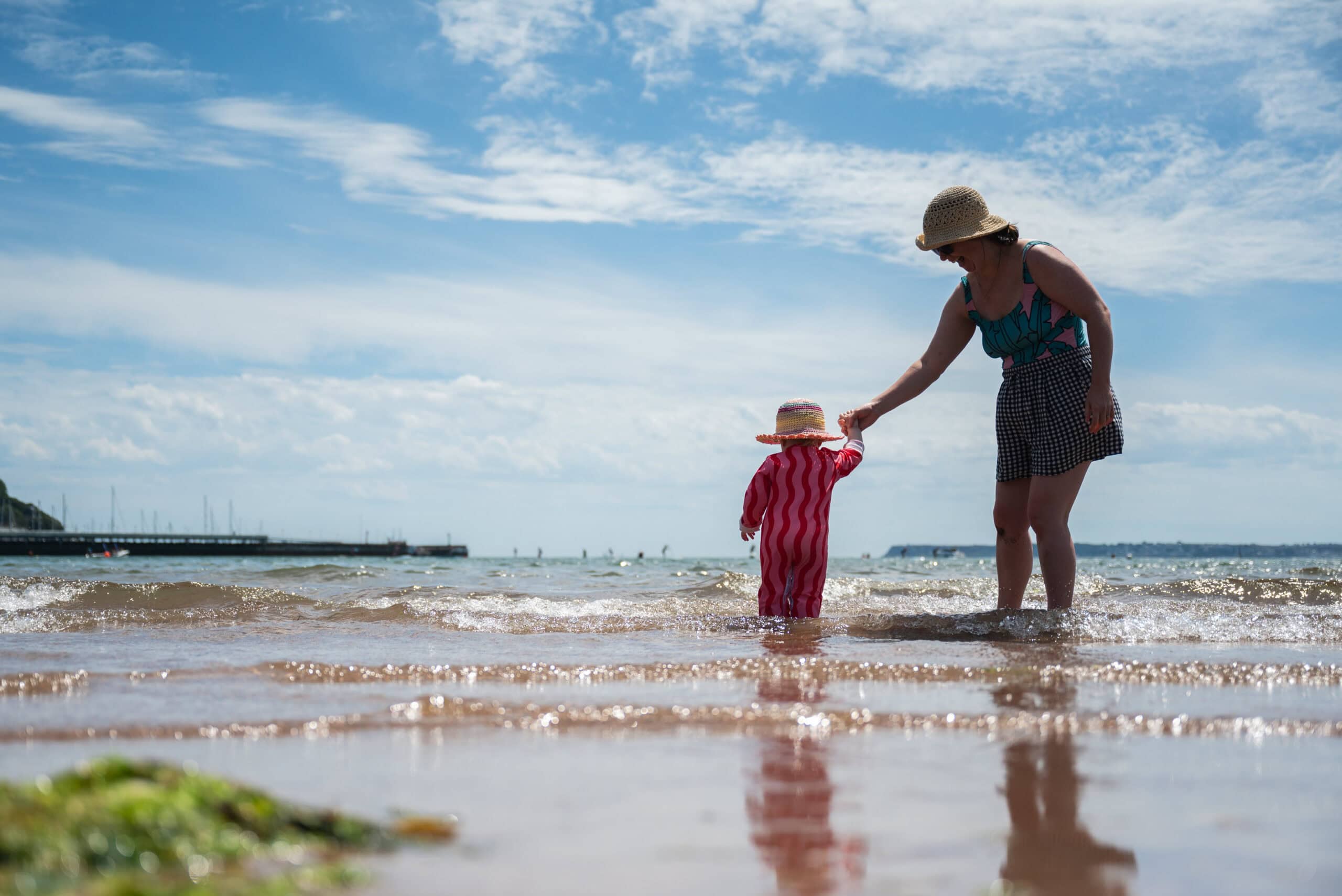 Mum and her toddler paddle in the sea on a sunny day