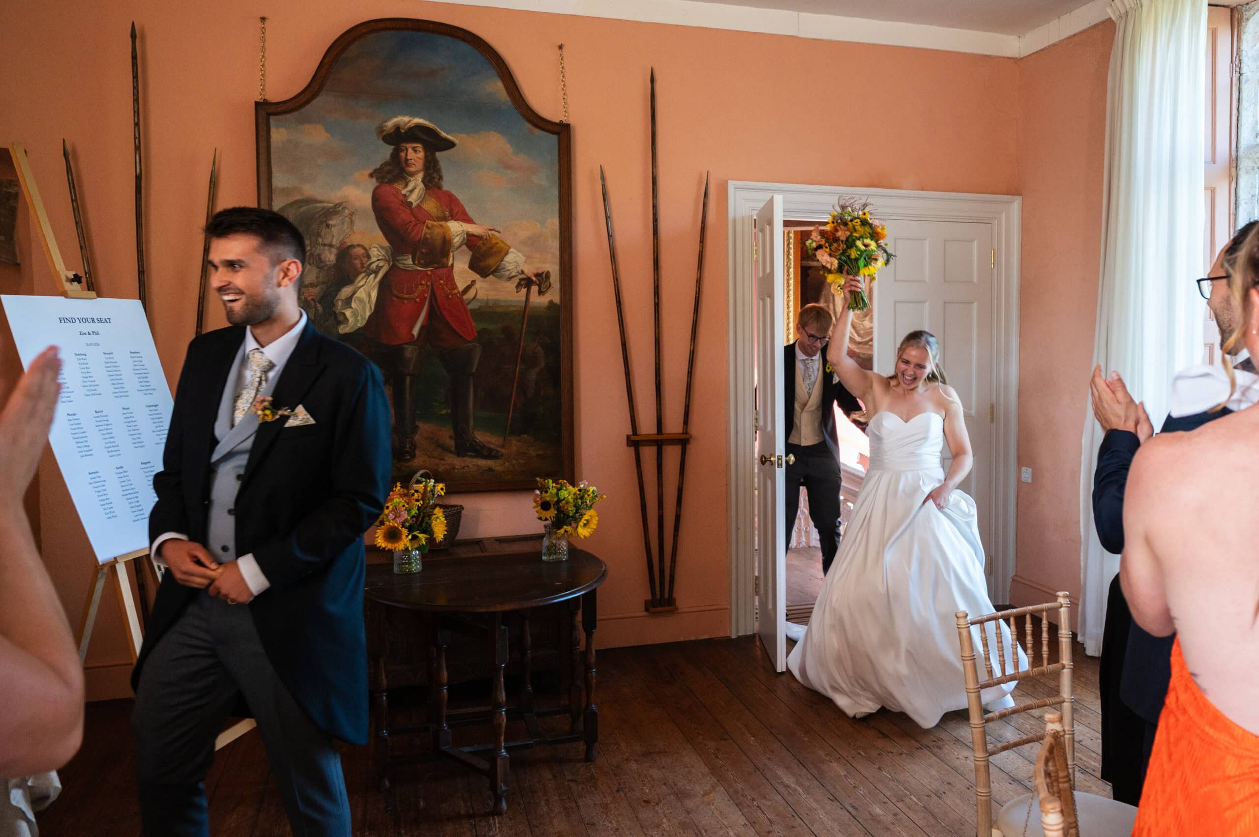 A bride walking into the dining room at Holme Pierrepont Hall as the groom waits beside a large oil painting.