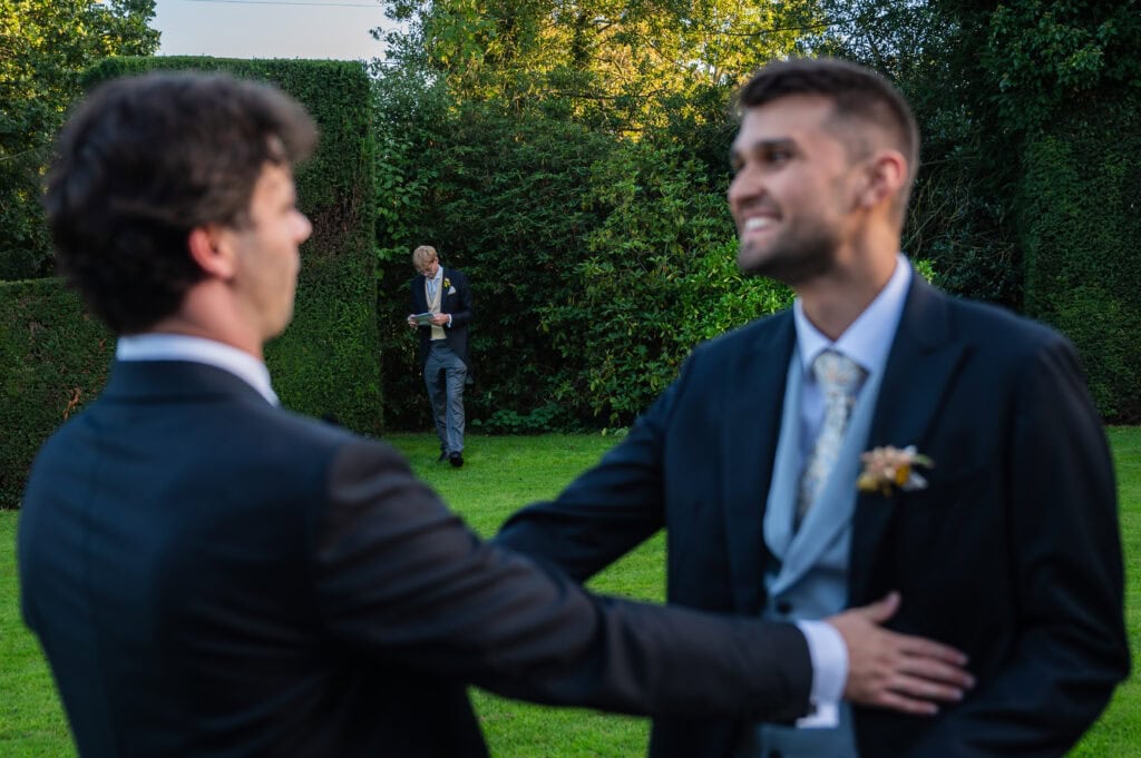 Two groomsmen greeting each other on the hedged back lawn at Holme Pierrepont Hall.
