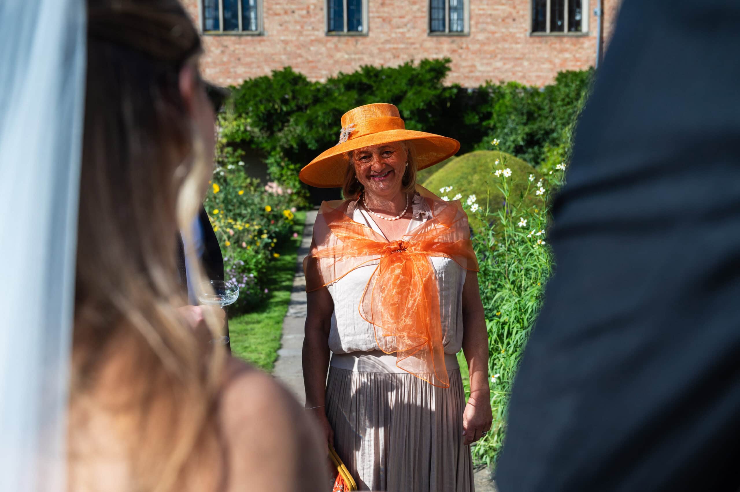A wedding guest in an orange hat among the flowers of the walled courtyard garden at Holme Pierrepont Hall.