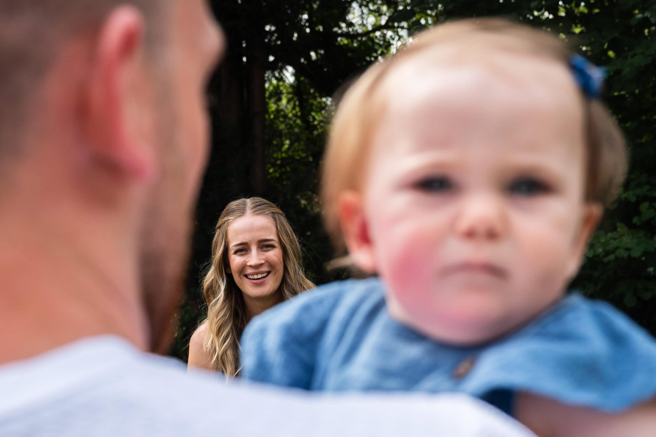 A baby looks at the camera as mum smiles behind at a family gathering