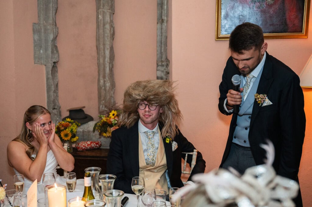 The groom wearing a Tina Turner wig while the best man gives his speech at Holme Pierrepont Hall.
