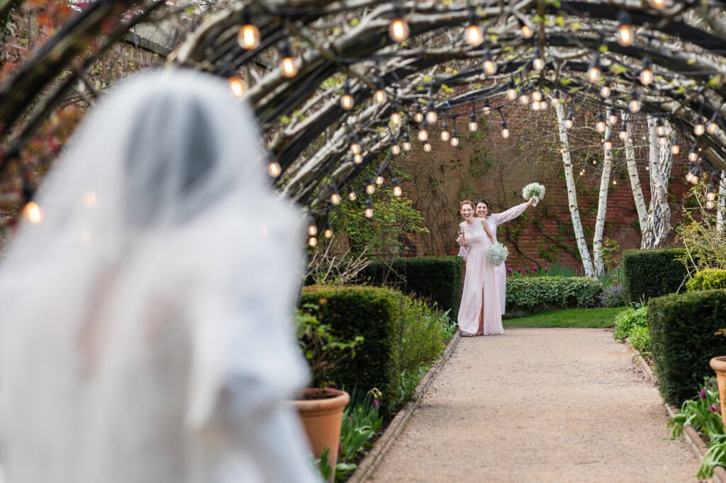 The Bramley apple arch strung with festoon lights, a bridesmaid waiting at the far end of the path
