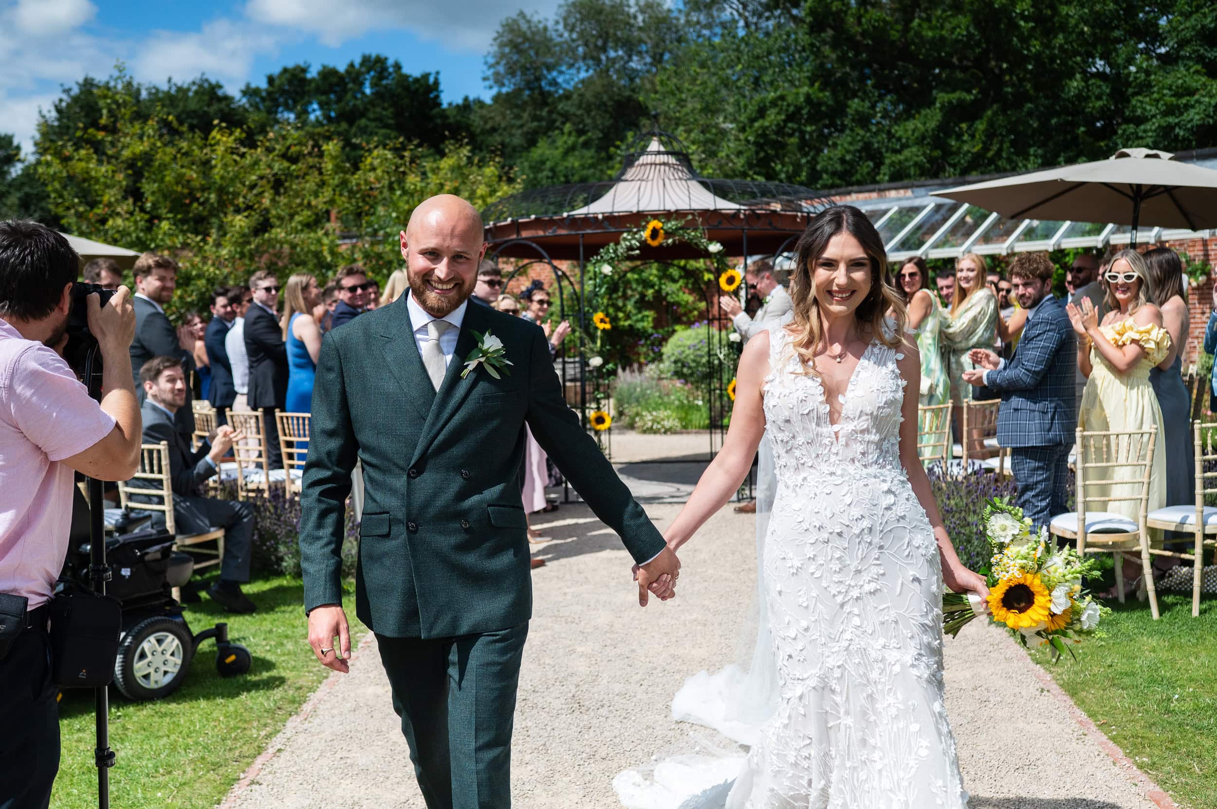 Bride and groom walking back down the aisle from the bandstand at Pippley Walled Garden as their guests applaud