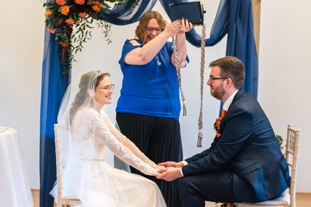 Celebrant Leni Robson lifting the handfasting cords over Megan and Will's joined hands at Rufford Mill
