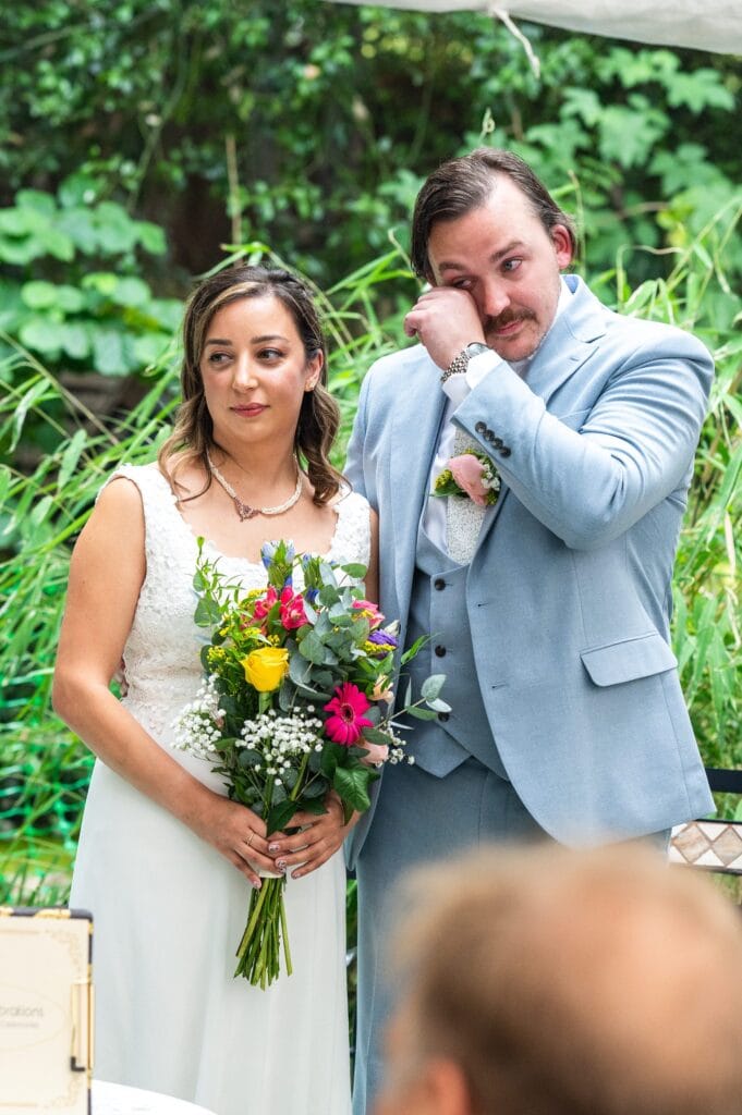 Tim wiping away tears beside Sabrina during their garden wedding ceremony in Beeston