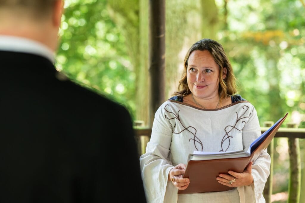 Celebrant Eva Greenslade in a white medieval-style dress leading a woodland wedding at Cedar Hollow