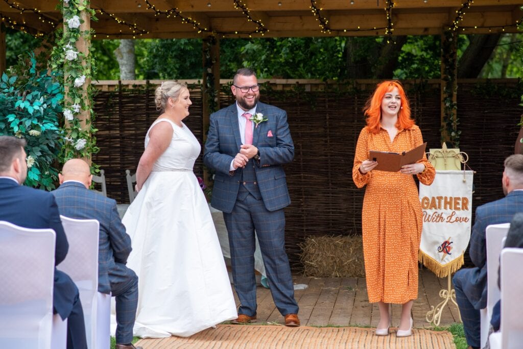 Celebrant Louise leading Alice and Keiron's ceremony under a wooden pergola at Overgrown Acres, Cotgrave