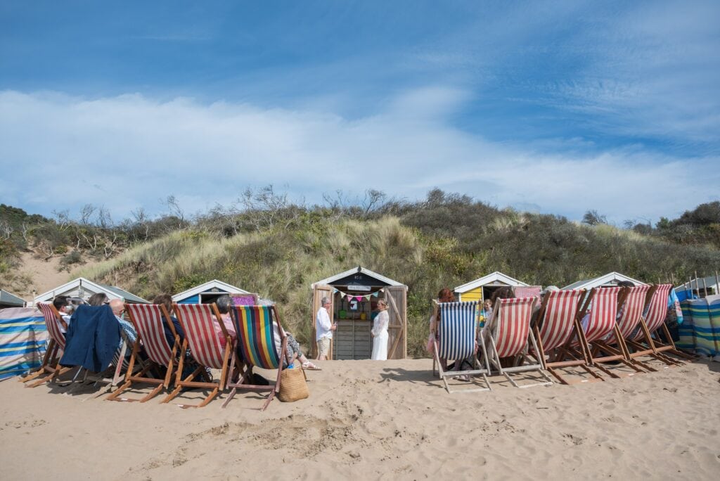 Guests in striped deckchairs watching a beach wedding ceremony at Saunton Sands, North Devon