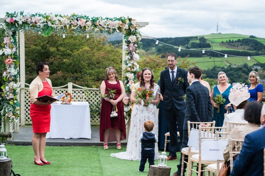 Celebrant Number 1 leading Leila and Steve's ceremony under a floral arch at The Stables Wedding Farm
